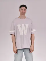 Remera gris de corte oversize con cuello redondo, mangas cortas con doble raya blanca y estampa frontal de una letra "W" grande en color blanco con efecto desgastado.