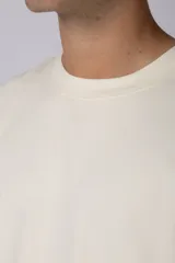 Remera de corte oversize en color crudo, con cuello redondo y mangas cortas. Presenta un pequeño estampado gráfico minimalista en el lado derecho del pecho.