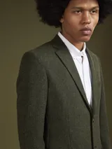Blazer de corte clásico en color verde oliva con textura jaspeada. Presenta solapas de muesca y cierre frontal con botones.