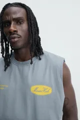 Musculosa de corte relajado con efecto lavado, cuello redondo y sisas amplias. Presenta estampados gráficos en color amarillo en el frente y acabados irregulares que le otorgan una apariencia única.