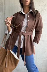 Sobrecamisa de gamuza color chocolate, con cierre frontal de botones metálicos y lazo ajustable en la cintura. Presenta cuello clásico y mangas largas con puños rectos.