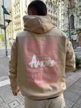 Canguro con capucha color beige, de corte oversize, con estampa gráfica en la espalda que repite la palabra 'Amore' en tonos rosados y blancos.