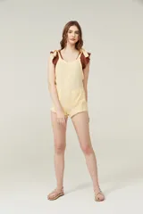 Mono corto color amarillo pastel, con breteles finos que se atan en los hombros, escote recto y dos bolsillos delanteros.