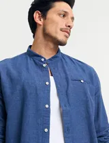 Camisa de cuello mao y manga larga, confeccionada en una mezcla de lino y algodón. Presenta un diseño de corte recto con botones en tono natural y un bolsillo pequeño en el pecho.
