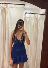 Vestido corto negro con estampado de plumas doradas, escote en V, breteles finos cruzados en la espalda, cut-outs laterales y volado en el ruedo.