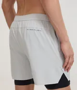 Bermuda deportiva verde militar con short de compresión incorporado, cintura elástica y cordón ajustable, confeccionada en microfibra de poliéster y elastano.