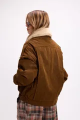 Campera de gamuza negra con cuello de piel sintética en color crema, cierre frontal, corte oversize y diseño estructurado con hombreras.