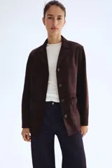 Campera tipo blazer o chaqueta de tejido suave con acabado cepillado, color marrón oscuro. Presenta solapas de muesca, cierre frontal de tres botones y dos bolsillos parche grandes en la parte delantera inferior.