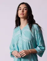 Camisa celeste con estampado de cachemir en blanco, cuello a la base, escote en V y abertura central con botones. Terminación de ruedo asimétrico. Manga 3/4 de largo regulable con presilla y botón.