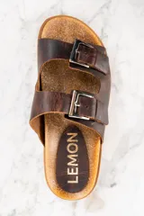 Sandalias de cuero marrón con doble tira ajustable con hebilla metálica.