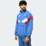Buzo tipo rompevientos de nylon con medio cierre frontal, cuello alto y puños elásticos. Presenta un diseño en bloques de color azul, blanco y bordó, con el escudo del Club Nacional de Football y el logo de Umbro estampados en el pecho.