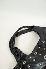 Bolso negro con asas redondas y diseño decorado con ojales y tachas metálicas.