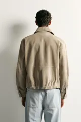 Cazadora relaxed fit de piel y ante color beige, con cuello solapa, manga larga con puño, bolsillos delanteros con solapa y cierre frontal oculto con cremallera y botones a presión.