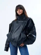 Chaqueta de efecto piel en color negro con acabado granulado, diseño de silueta relajada, cuello alto estructurado y cierre asimétrico.