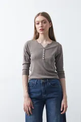 Remera de manga larga color beige, confeccionada en algodón, con escote en V y cartera corta de botones blancos.