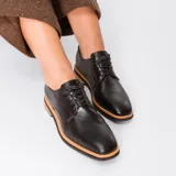 Zapato mocasín de cuero vacuno color negro, con cordones y punta redonda. Tiene taco de madera foliado en cuero de 2,5 cm y entre suela de goma de 1 cm.