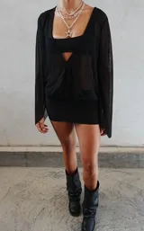 Vestido corto negro de diseño ajustado, con escote pronunciado y mangas largas acampanadas de tela semitransparente.