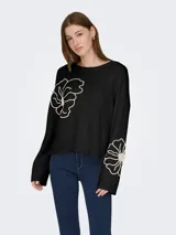 Sweater de punto color negro con cuello redondo y mangas largas. Presenta un diseño bordado de flores en color crema, ubicado en la parte superior del frente y en el puño de una de las mangas.