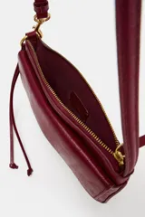 Bolso de hombro color bordó, con asa de hombro, bolsillo exterior con solapa y cierre de imán, y cierre principal con cremallera. Incluye detalle de anilla metálica dorada y tira con nudos en el lateral.