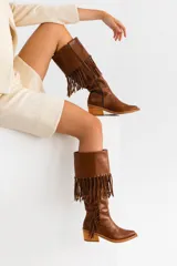 Bota tejana de cuero color marrón, con caña alta con flecos, taco de madera foliado en cuero y cierre lateral.