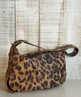 Bolso de hombro tipo hobo con acabado texturizado efecto craquelado en tonos beige y blanco. Cuenta con una correa ajustable con hebilla metálica, cierre superior y diseño espacioso.