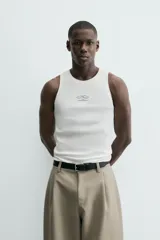 Camiseta tipo tank (sin mangas) de corte relaxed fit, color blanco, con cuello redondo y un pequeño estampado gráfico en el pecho que dice "SANTA BARBARA EST. 1987 CALIFORNIA".