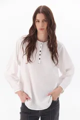Blusa blanca de corte clásico con pespuntes negros a contratono, cuello con botones y tajos laterales.