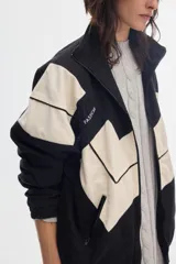 Campera oversize de denim en color negro y crudo, con diseño geométrico en bloques, cuello alto, cierre frontal y bolsillos.