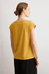 Remera mostaza de manga corta con detalles de encaje bordado (broderie) en los hombros, cuello redondo y corte recto.