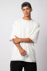 Remera de corte oversize color malva, confeccionada en algodón pesado, con costuras externas visibles en color blanco que recorren el centro, el cuello y los bordes de las mangas.