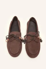 Mocasín estilo náutico de gamuza marrón, con cordones de cuero, borla decorativa y cuentas de colores en el empeine.
