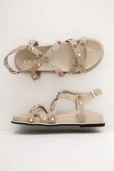 Sandalias de cuero color beige, con tiras cruzadas en el empeine decoradas con tachas y esferas doradas, base anatómica y pulsera ajustable al tobillo.