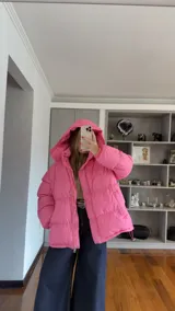 Campera puffer de corte holgado en color beige, con diseño acolchado, cuello alto y capucha desmontable. Cuenta con cierre frontal y botones a presión, además de puños elásticos.