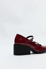 Zueco estilo Mary Jane color negro charol, con doble tira y hebillas metálicas. Presenta punta cuadrada y taco ancho de altura media.