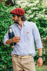 Camisa celeste de manga larga con cuello clásico, cierre frontal con botones de madera y un bolsillo en el pecho con aplique de etiqueta marrón.