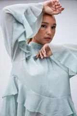 Blusa de gasa color verde agua, con cuello alto fruncido, mangas largas acampanadas y diseño con volados en el frente y hombros.