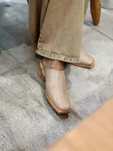 Zuecos color beige con diseño bordado en el empeine, taco de madera y punta cuadrada.
