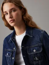 Campera de denim rígido color azul índigo oscuro, con corte cropped y ajuste auténtico de los 90. Presenta cuello en punta, bolsillos con solapa en el pecho y botones metálicos de la marca. Incluye una insignia con el logo de Calvin Klein en el bolsillo del pecho.