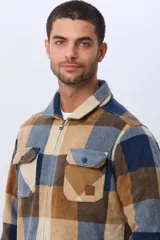 Campera leñadora de tejido polar con estampado a cuadros en tonos marrones, beige y azules. Presenta cierre frontal, cuello camisero, bolsillos superiores con solapa y bolsillos laterales.