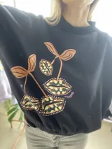 Buzo cropped de algodón color verde militar, con mangas ranglan y diseño estampado en el frente con motivos de besos y moños. Cuenta con elástico holgado en la cintura y los puños.