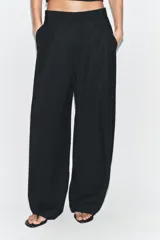 Pantalón negro de tiro alto y pernera ancha, confeccionado en tejido fluido, con bolsillos laterales y detalles de pliegues en la parte delantera.