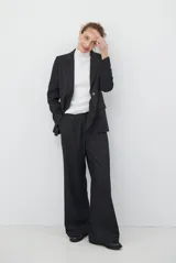 Blazer de corte sastrero en color gris oscuro, con cierre frontal de un botón, solapas clásicas y bolsillos con solapa. Presenta una estructura entallada y hombreras marcadas.