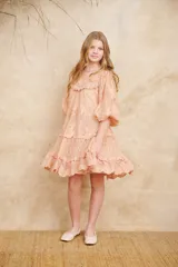 Vestido corto de encaje color durazno, con diseño de volados en capas, mangas largas abullonadas y cuello redondo con detalles bordados.