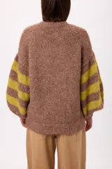 Buzo de tejido de punto con textura peluda, de corte holgado y mangas amplias. Presenta un diseño geométrico con una flor grande estampada en el centro, combinando tonos fucsia, rosa y marrón en un patrón de bloques y rayas.