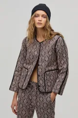 Chaqueta de jacquard color beige con estampado damasco en negro, corte boxy, vivos negros a contratono, amplios bolsillos frontales y botones a presión escondidos.
