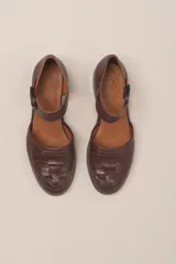 Zapato de cuero color borgoña, con puntera redondeada y diseño trenzado. Presenta una tira sobre el empeine con hebilla metálica negra.