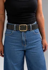 Cinto ancho negro con perforaciones rectangulares dobles, textura símil reptil y hebilla rectangular metálica de estilo envejecido.
