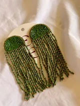 Caravanas largas de estilo artesanal, compuestas por una base semicircular bordada con mostacillas verdes y flecos colgantes de mostacillas verdes y doradas.
