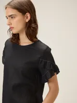 Blusa de lino color crudo, con cuello redondo y mangas cortas adornadas con volados dobles.