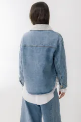 Campera de jean azul con detalles de tejido crochet en color blanco en el cuello y en uno de los bolsillos frontales. Posee cierre frontal con botones metálicos y un corte clásico.